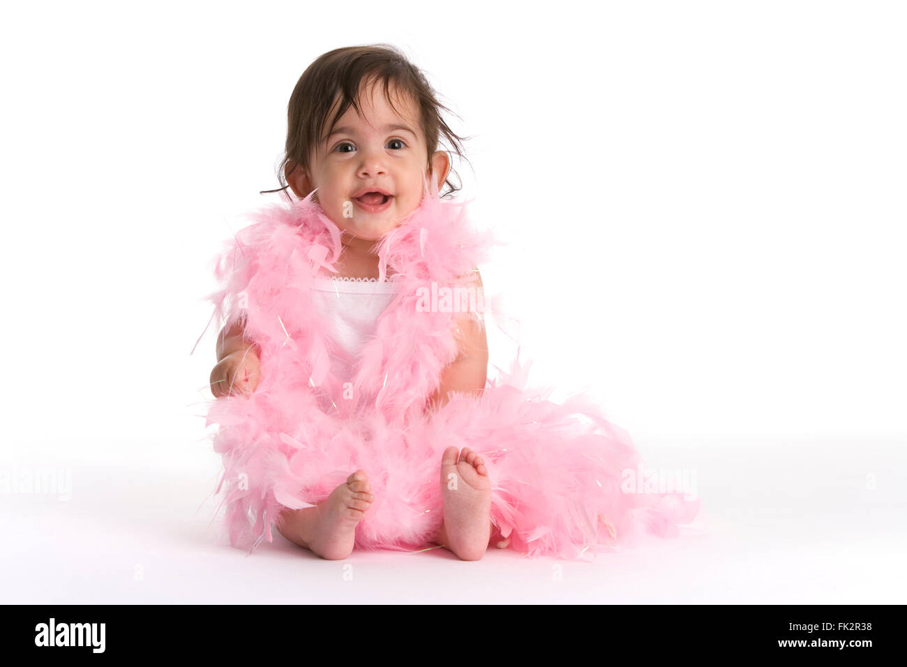 Baby ragazza seduta sul pavimento vestito in rosa piume come una diva su sfondo bianco Foto Stock