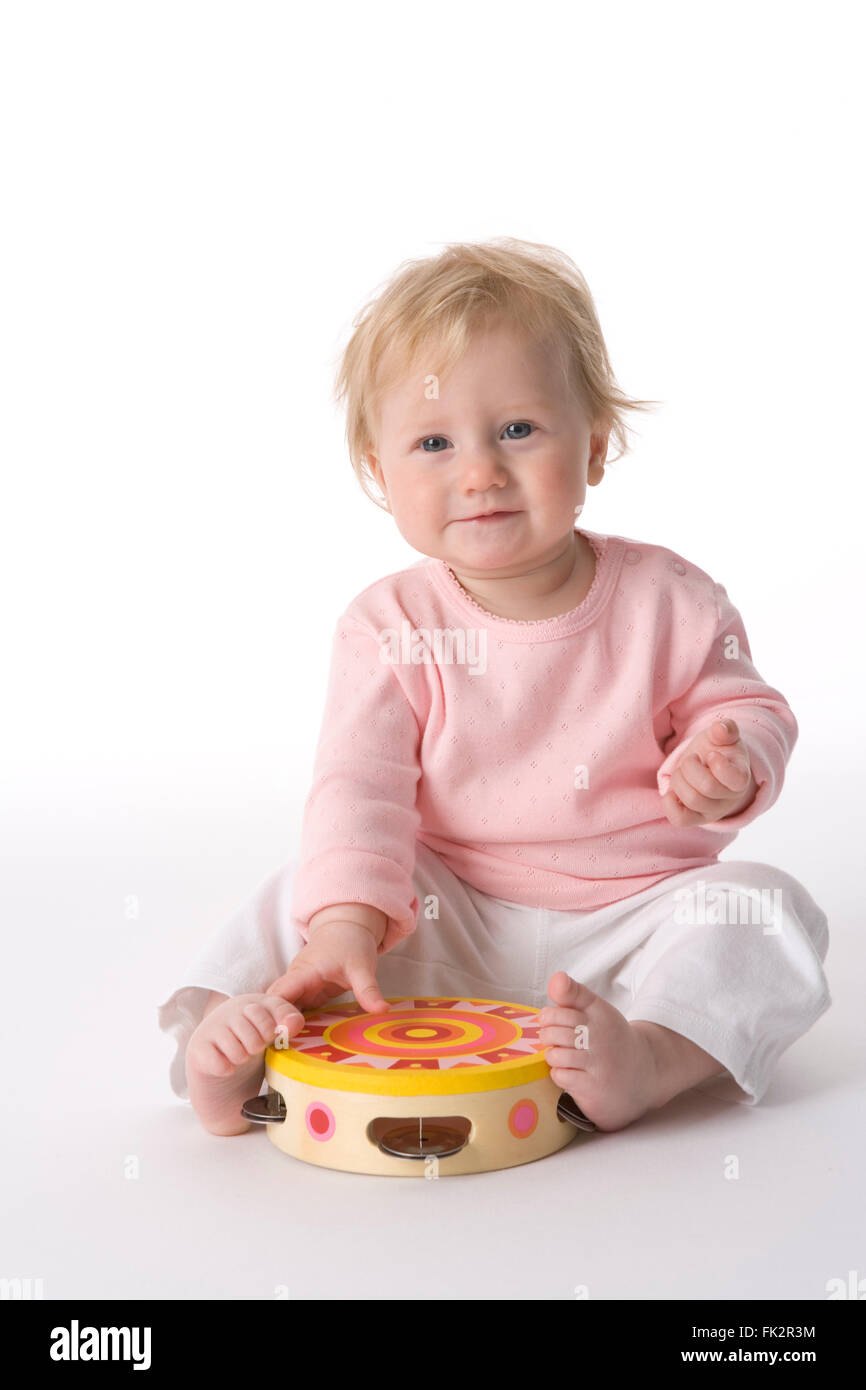 Baby ragazza seduta sul pavimento con un giocattolo tamburo su sfondo bianco Foto Stock