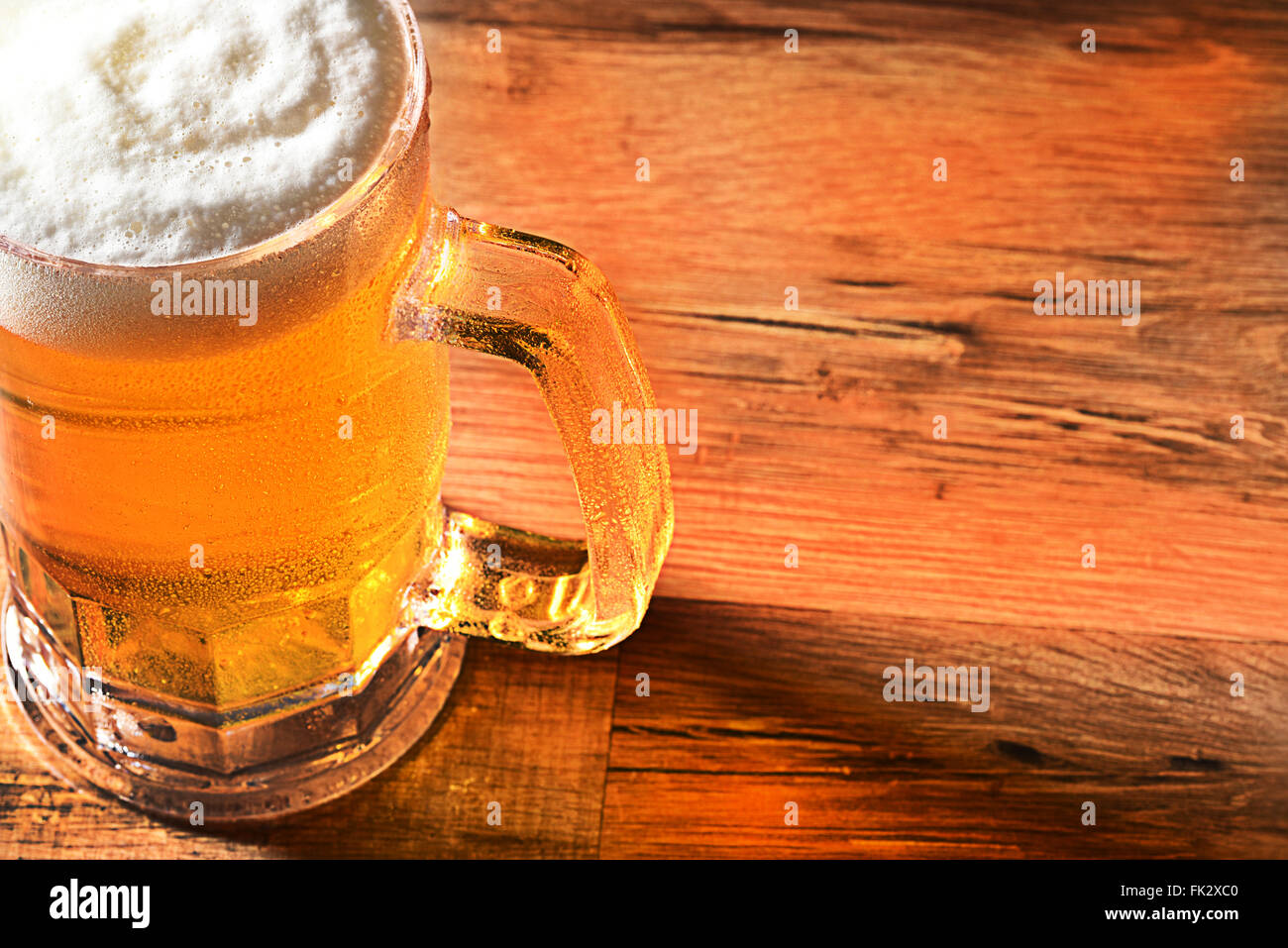 Primo piano di una birra fredda la tazza con una testa schiumoso e copia di spazio. Elevato angolo di visione con una calda luce laterale e riflessioni sulla tavola di legno. Foto Stock