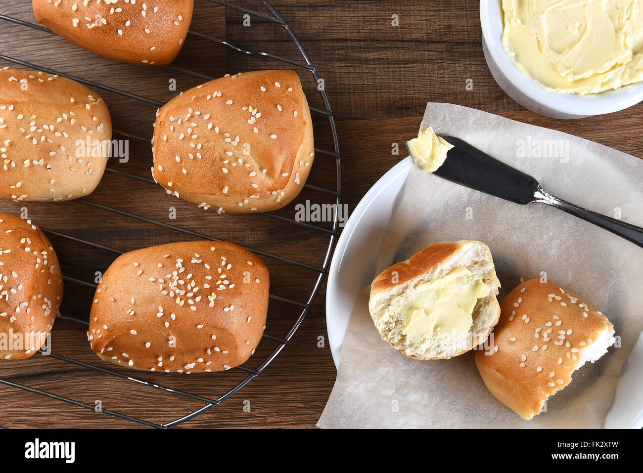 Angolo di alta vista di sesamo cena rotoli su un rack a filo con la piastra di pane e burro crock e il coltello. Foto Stock