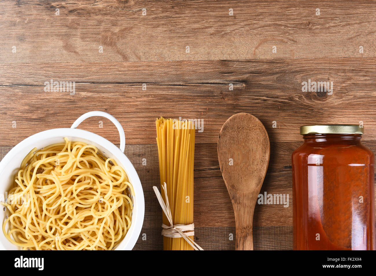 La cucina italiana ancora in vita con copia spazio. Woden cucchiaio, spaghetti secchi, la pasta cotta e un vaso di salsa su un legno tavolo da cucina. Foto Stock