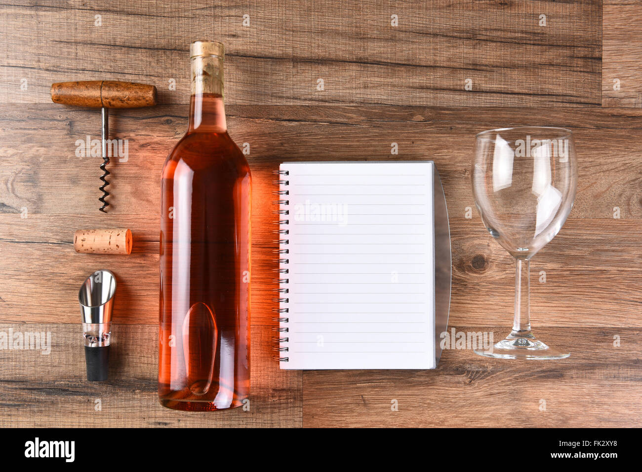Un elevato angolo di visione di una bottiglia di vino le note di degustazione notebook, cavatappi e bicchiere di vino su una tavola di legno. Foto Stock