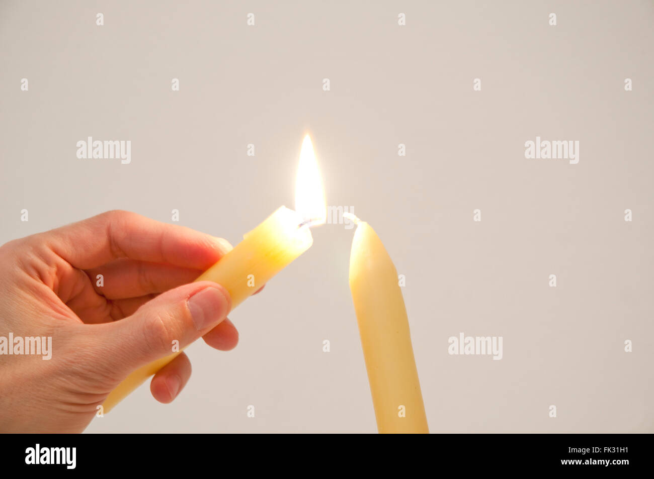 Mano d'uomo l'illuminazione di una nuova candela con una candela che brucia. Chiudere la vista. Foto Stock