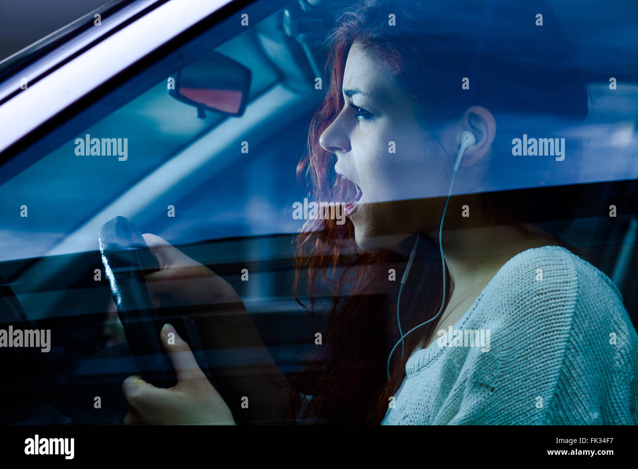 Urlando donna con gli auricolari alla guida di una macchina Foto Stock