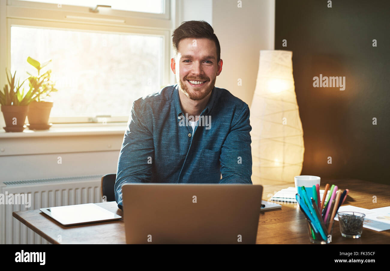 Imprenditore in ufficio con computer portatile guardando sorridente della fotocamera Foto Stock