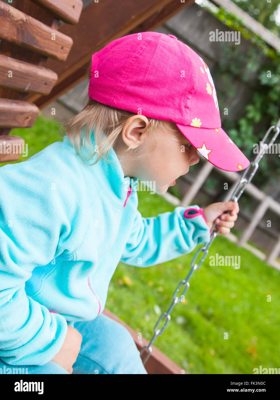 Outdoor ritratto di strani piccoli bambini in una rosa cappello da baseball su uno swing Foto Stock