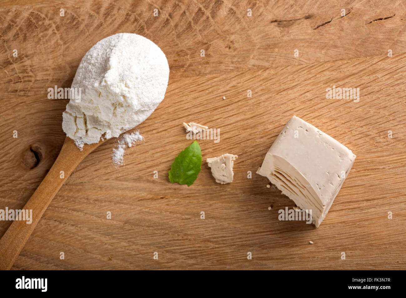 Il lievito sbriciolato cubo su una tavola di legno e un cucchiaio di farina bianca Foto Stock
