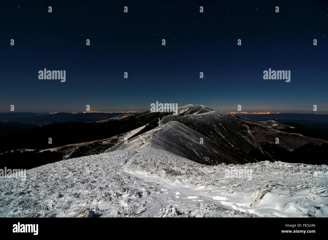 Luna splende su sentiero innevato oltre le creste di notte Foto Stock