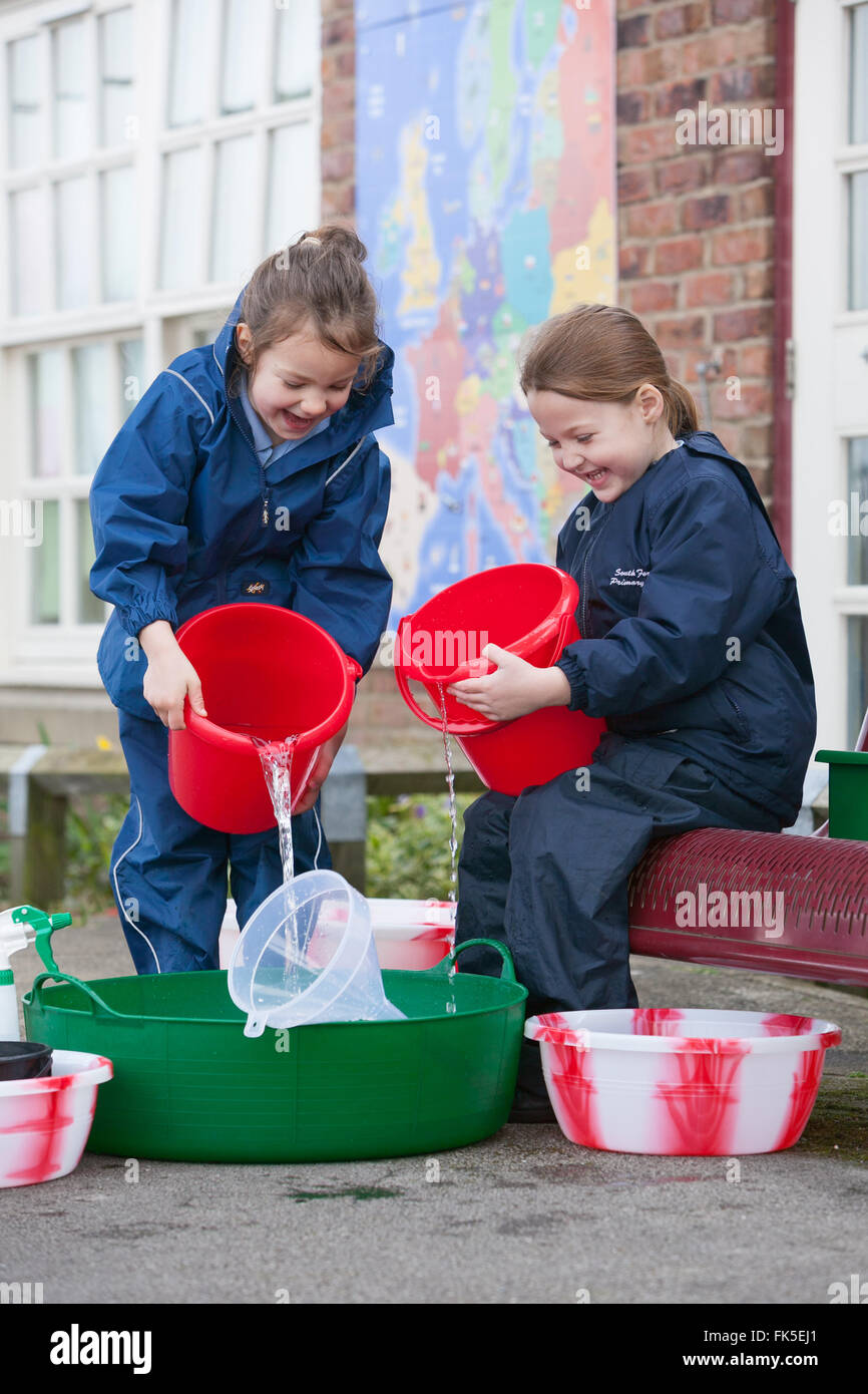 Due gli allievi della scuola primaria godendo i giochi d'acqua esterno utilizzando varie tazze e giocattoli. Foto Stock