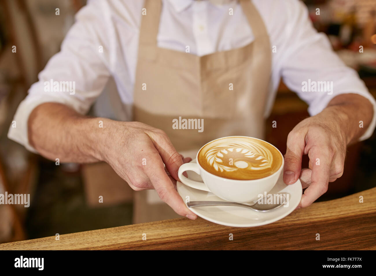 Close-up di uomo in grembiule che serve caffè permanente, mentre in coffee shop. Barista dandovi una tazza di caffè fresco presso il cafe. Foto Stock
