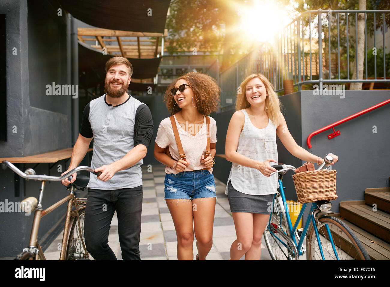 Tre giovani adulti camminare insieme avendo divertimento. I giovani con le biciclette passeggiate all'aperto in città. Foto Stock