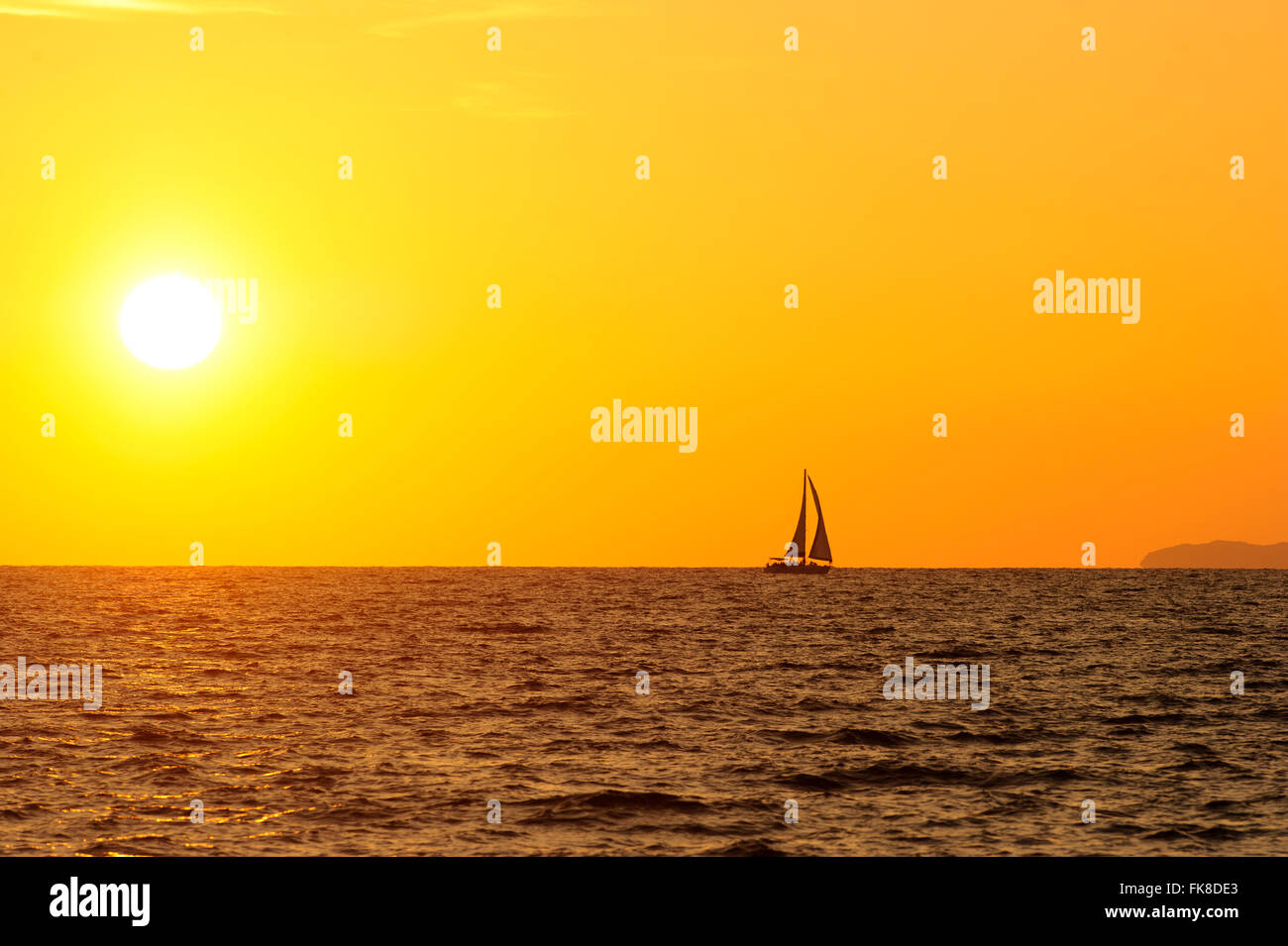 Barca a vela al tramonto è una silhouette di una barca a vela con un bianco caldo sole bruciante impostazione sull'oceano orizzonte contro un cielo arancione. Foto Stock