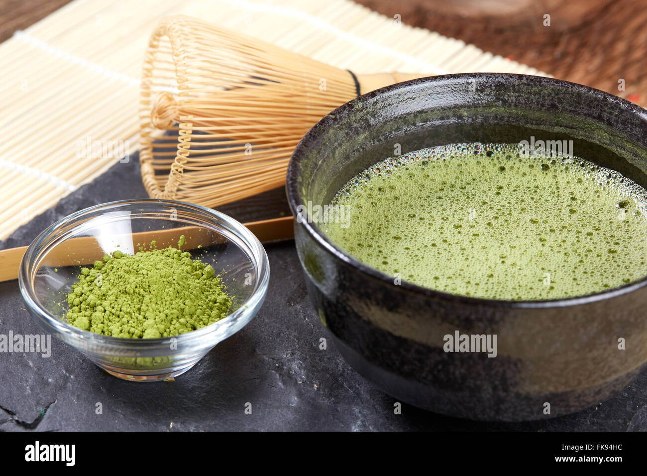 Verde matcha in polvere e tè e frusta e cucchiaio per la preparazione su pietra nera e piastra di Bianco di bambù tabella mat Foto Stock