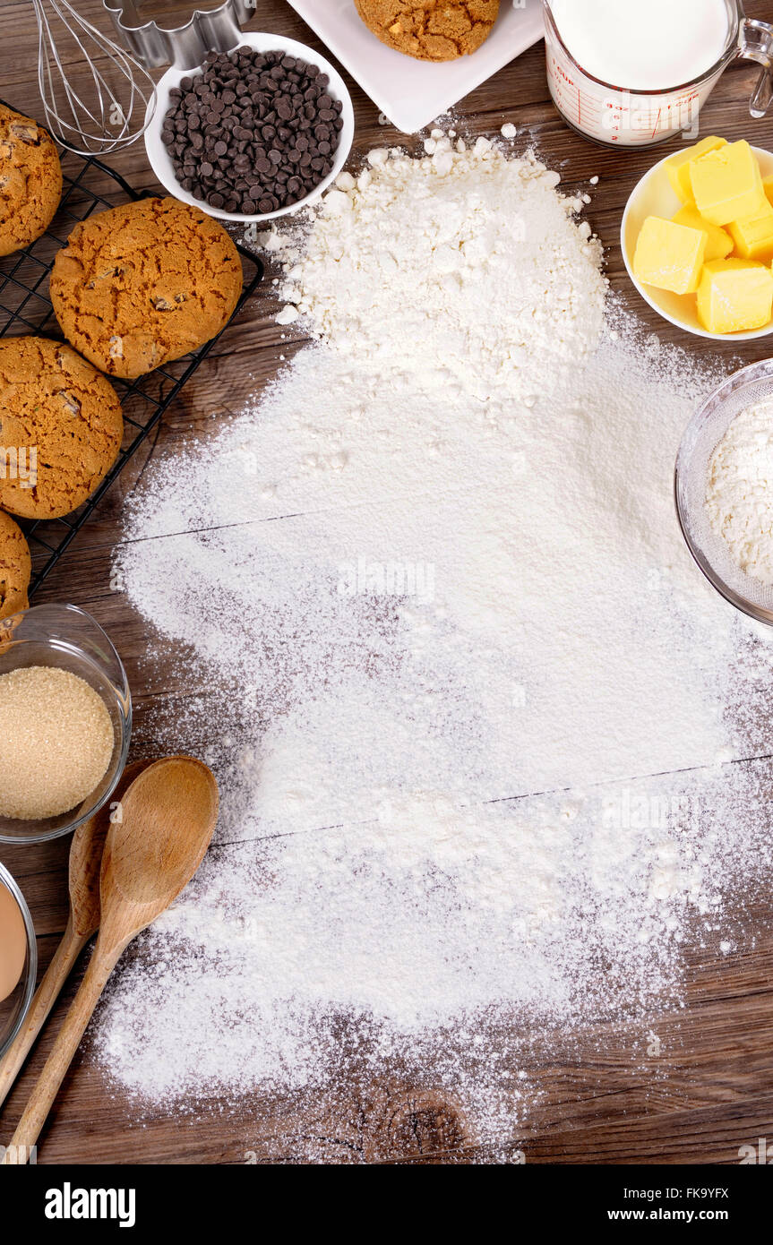 Appena sfornati i biscotti al cioccolato al buio su un tavolo di legno con spolverata di farina e ingredienti. Foto Stock