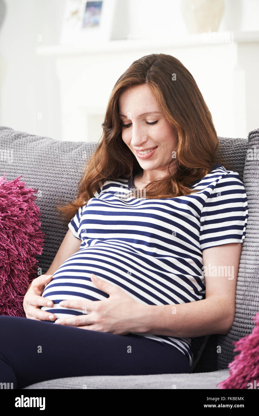 Donna incinta rilassante sul divano di casa Foto Stock