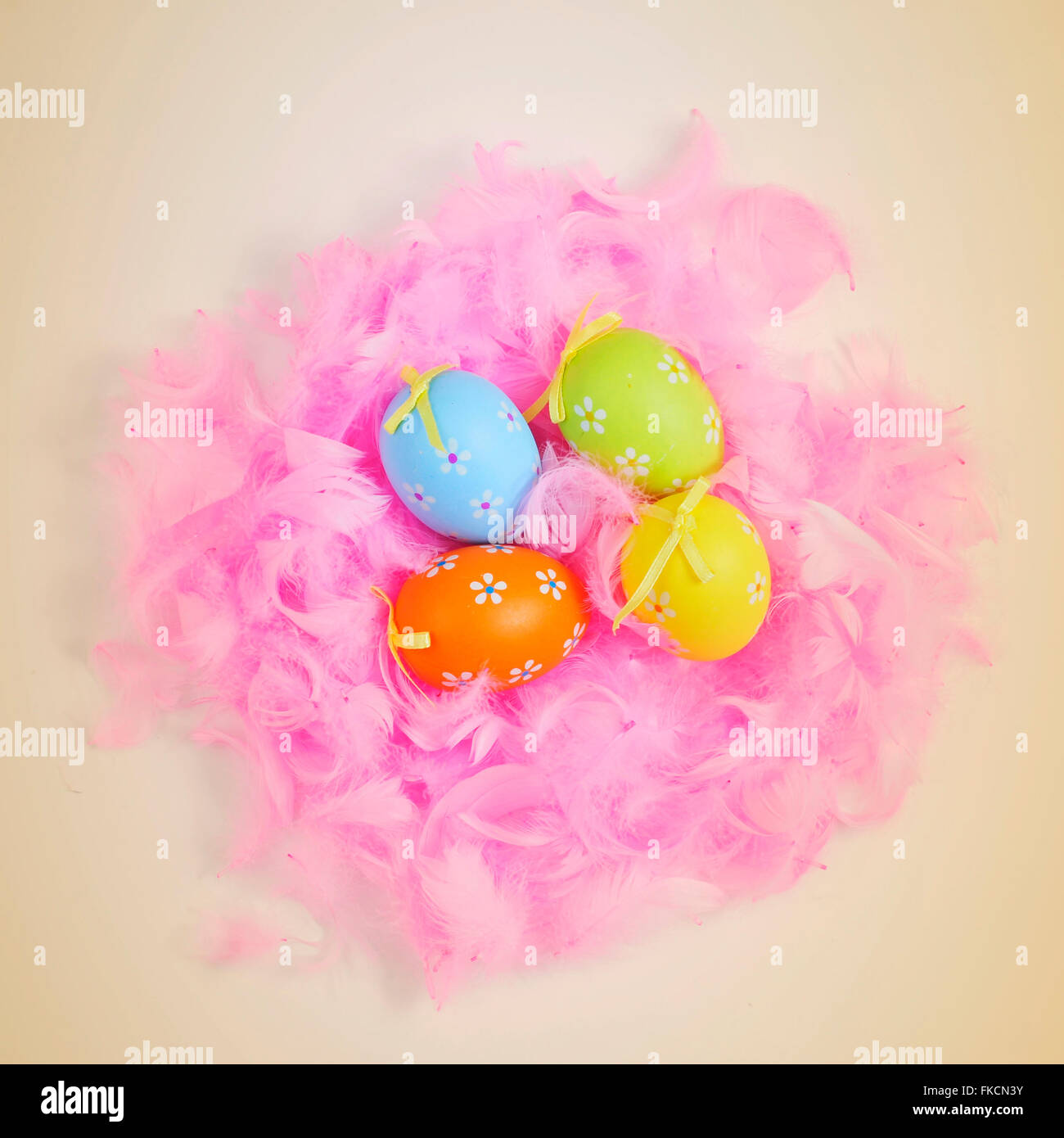 Alta angolazione di alcune decorate le uova di pasqua di diversi colori in un nido fatto con le piume rosa su sfondo beige Foto Stock