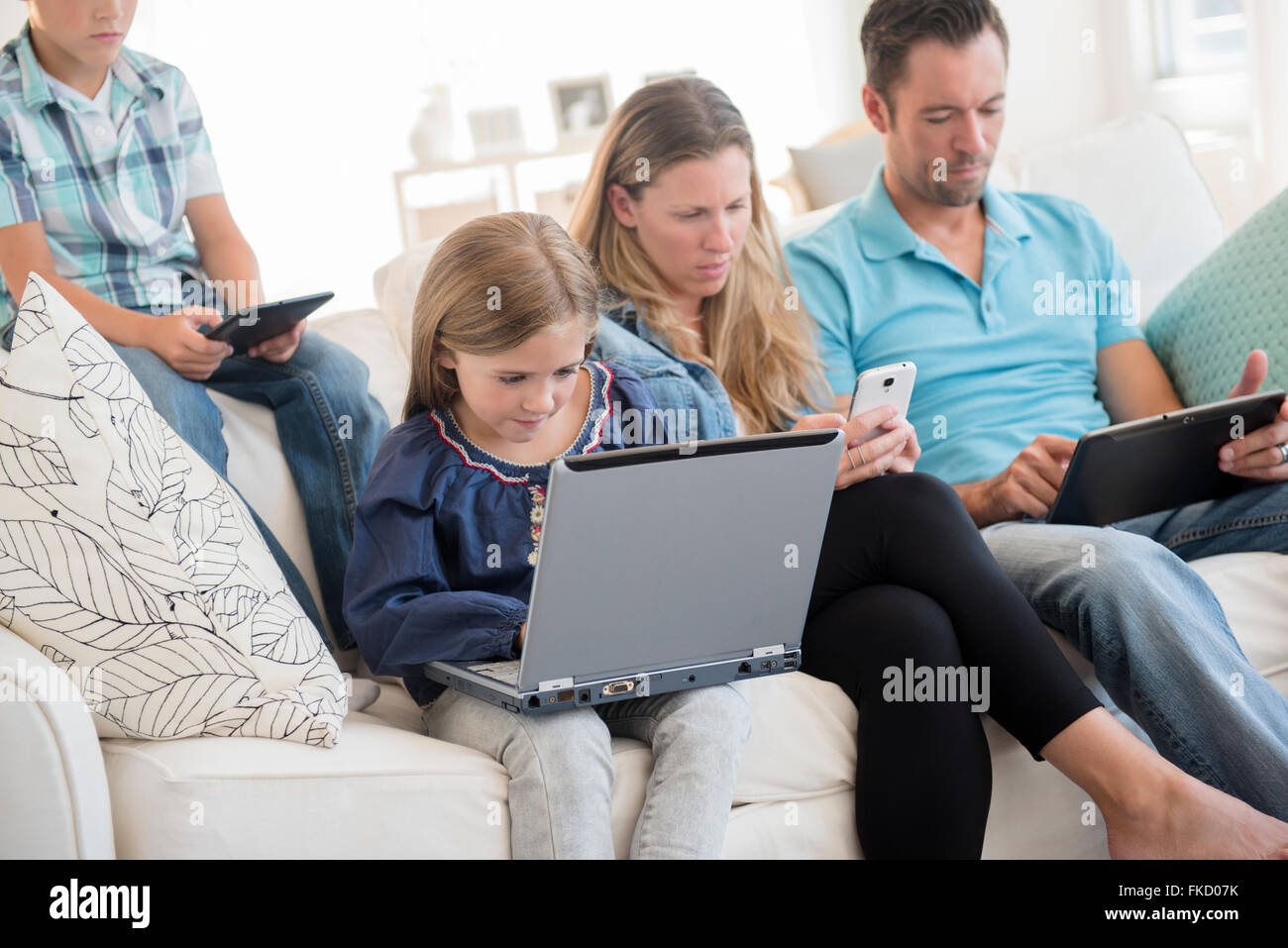 Famiglia con due bambini (6-7, 8-9) seduto sul divano, utilizzando laptop e tablet digitale Foto Stock