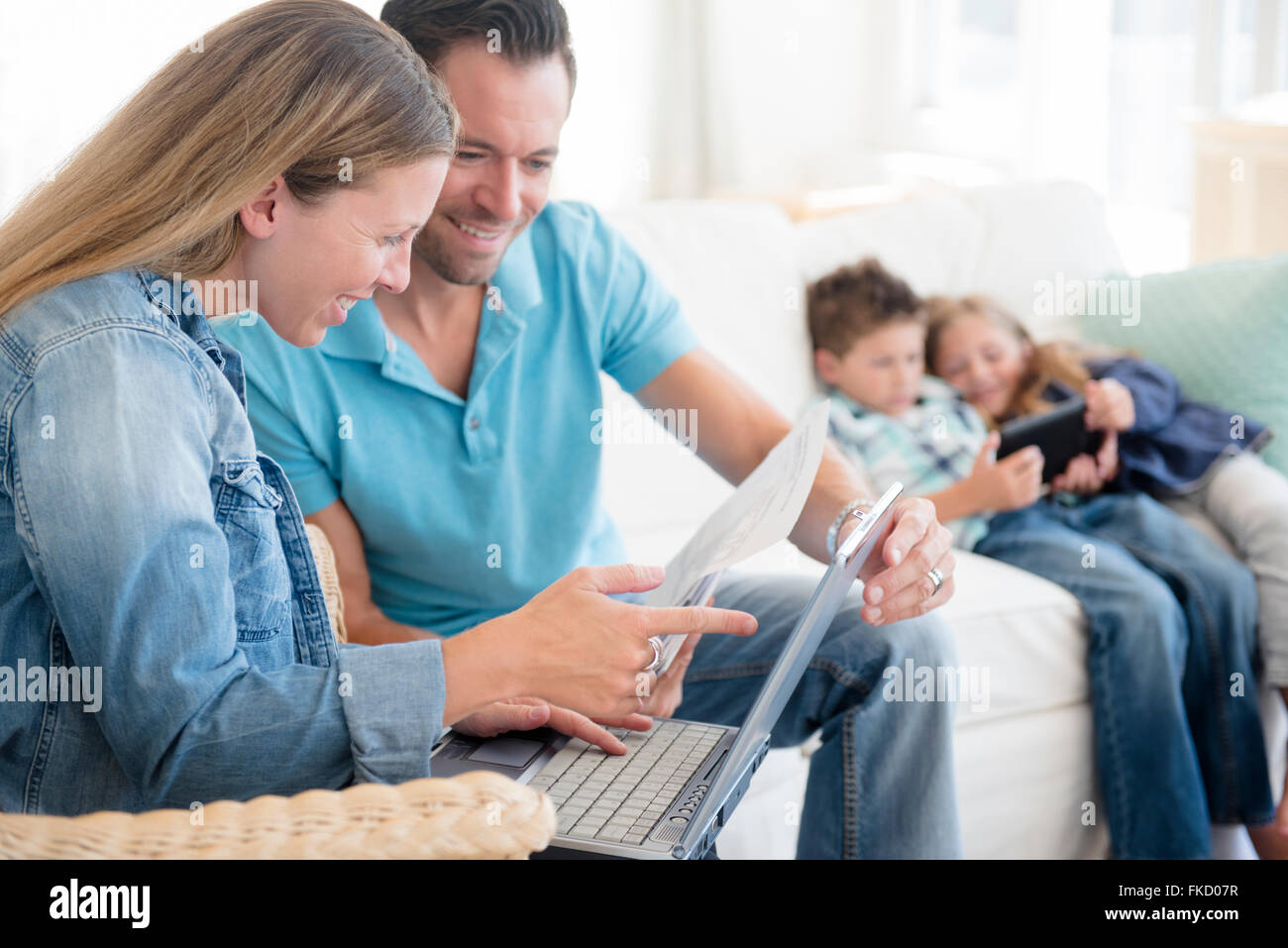L uomo e la donna il pagamento di fatture con due bambini (6-7, 8-9) seduto sul divano, utilizzando tavoletta digitale Foto Stock
