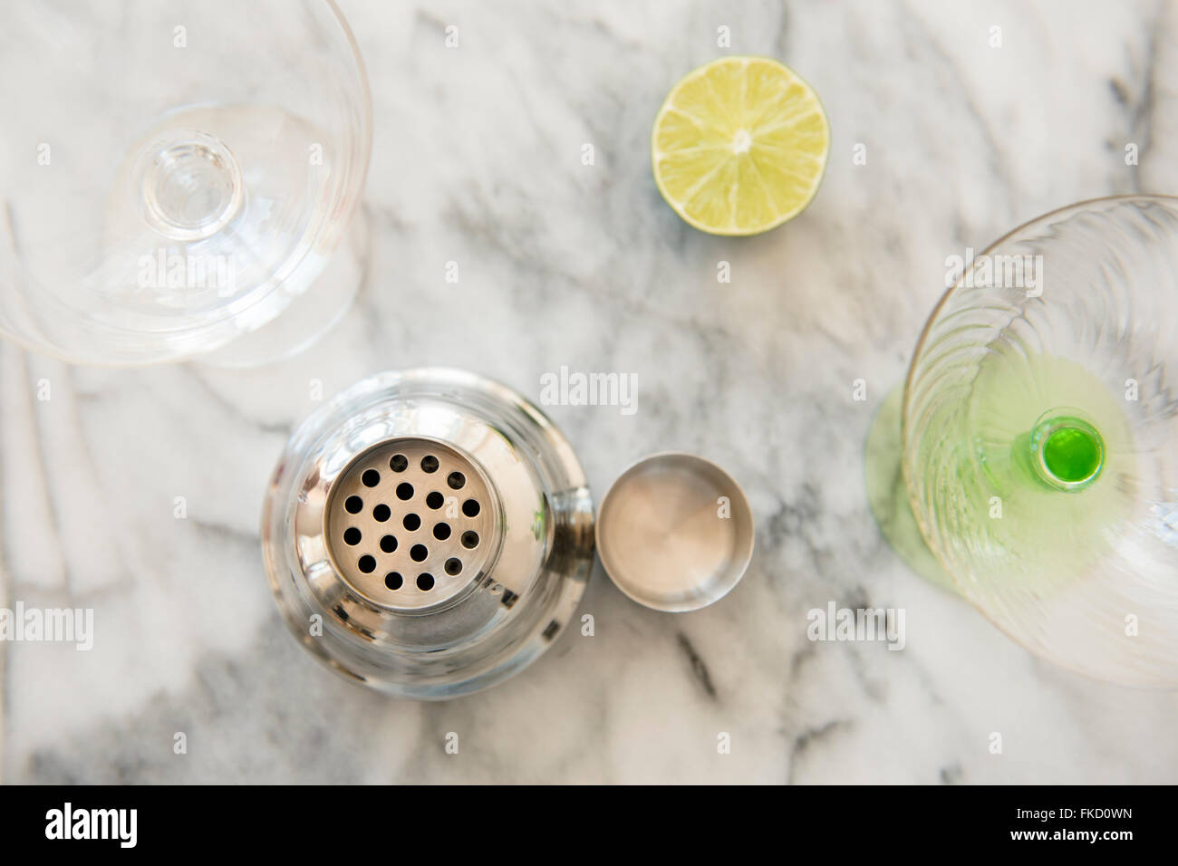 Cocktail in shaker, bicchieri da martini e dimezzato lime sul tavolo Foto Stock