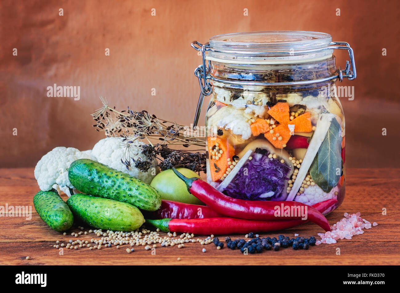 Jar assortiti di messi in salamoia lacto-fermentati sottaceti su un tavolo di legno circondato da spezie e verdure. Foto Stock