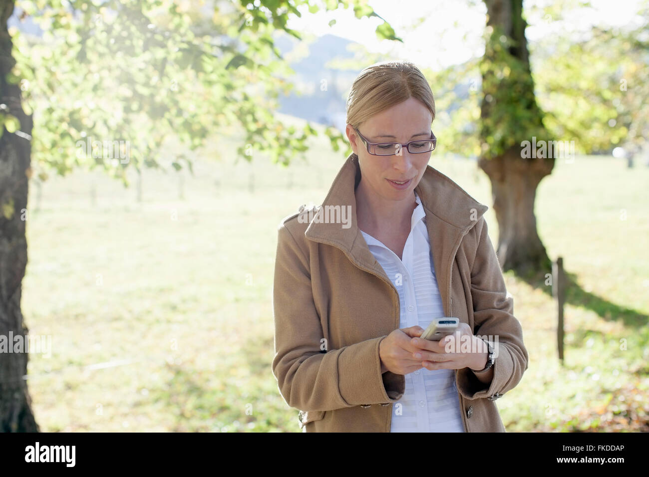 Donna in cappotto beige usando il telefono cellulare Foto Stock