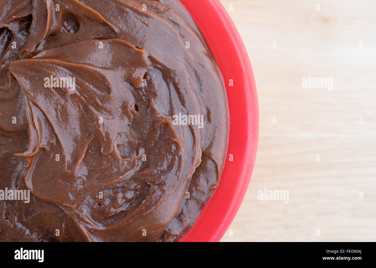 Top vista ravvicinata di una piccola ciotola riempita con salsa al cioccolato la glassa su una cucina in legno sul bancone. Foto Stock