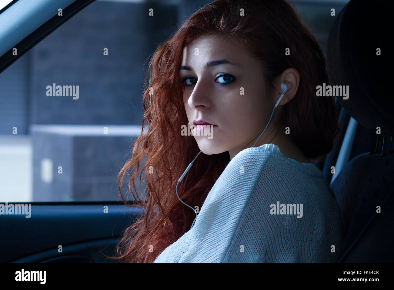 Redhead donna con auricolari seduti in auto Foto Stock