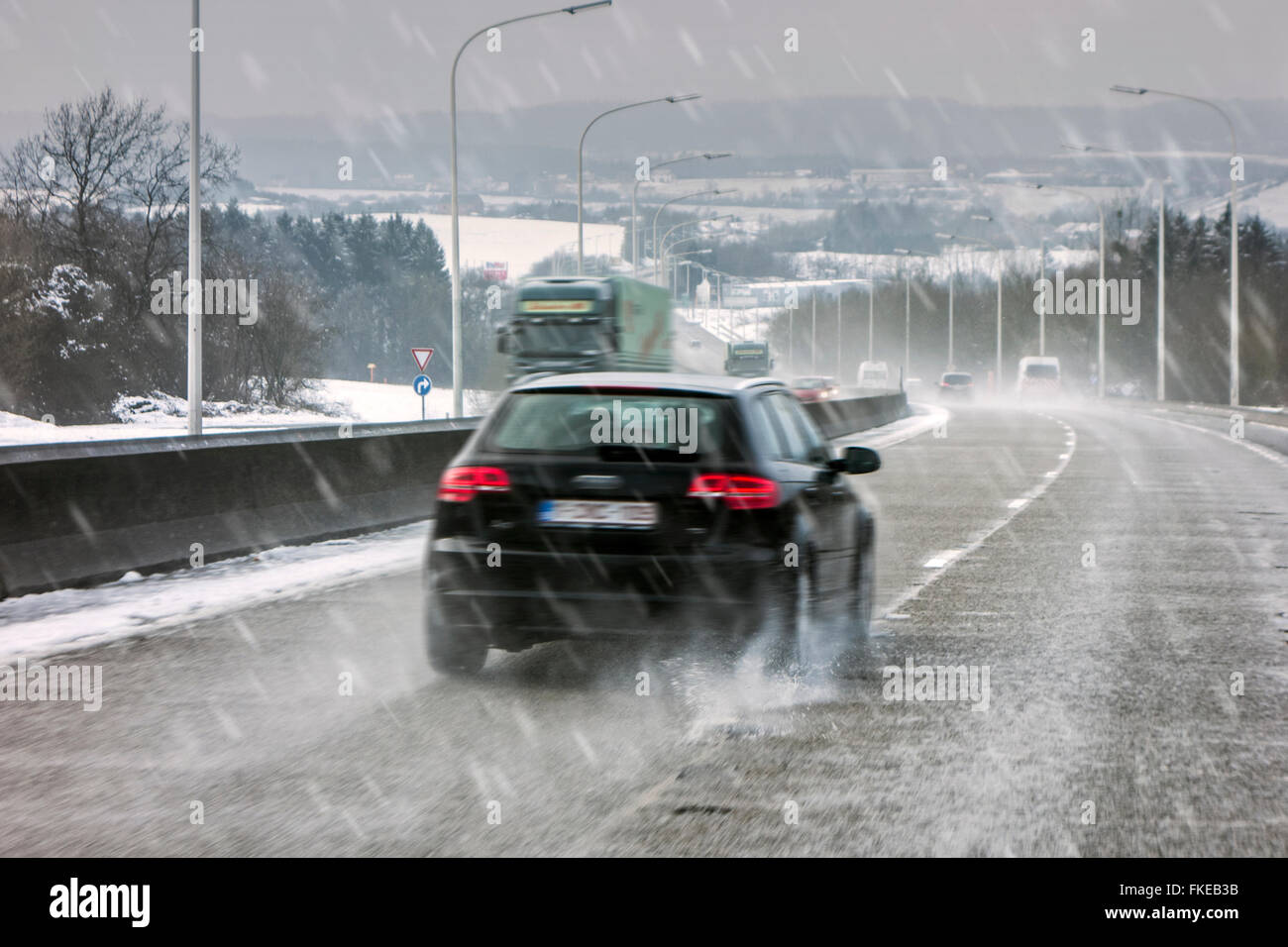 Vetture guida su autostrada sdrucciolevoli durante il nevischio causando pericolosi bagnato invernale le condizioni delle strade in inverno / molla Foto Stock