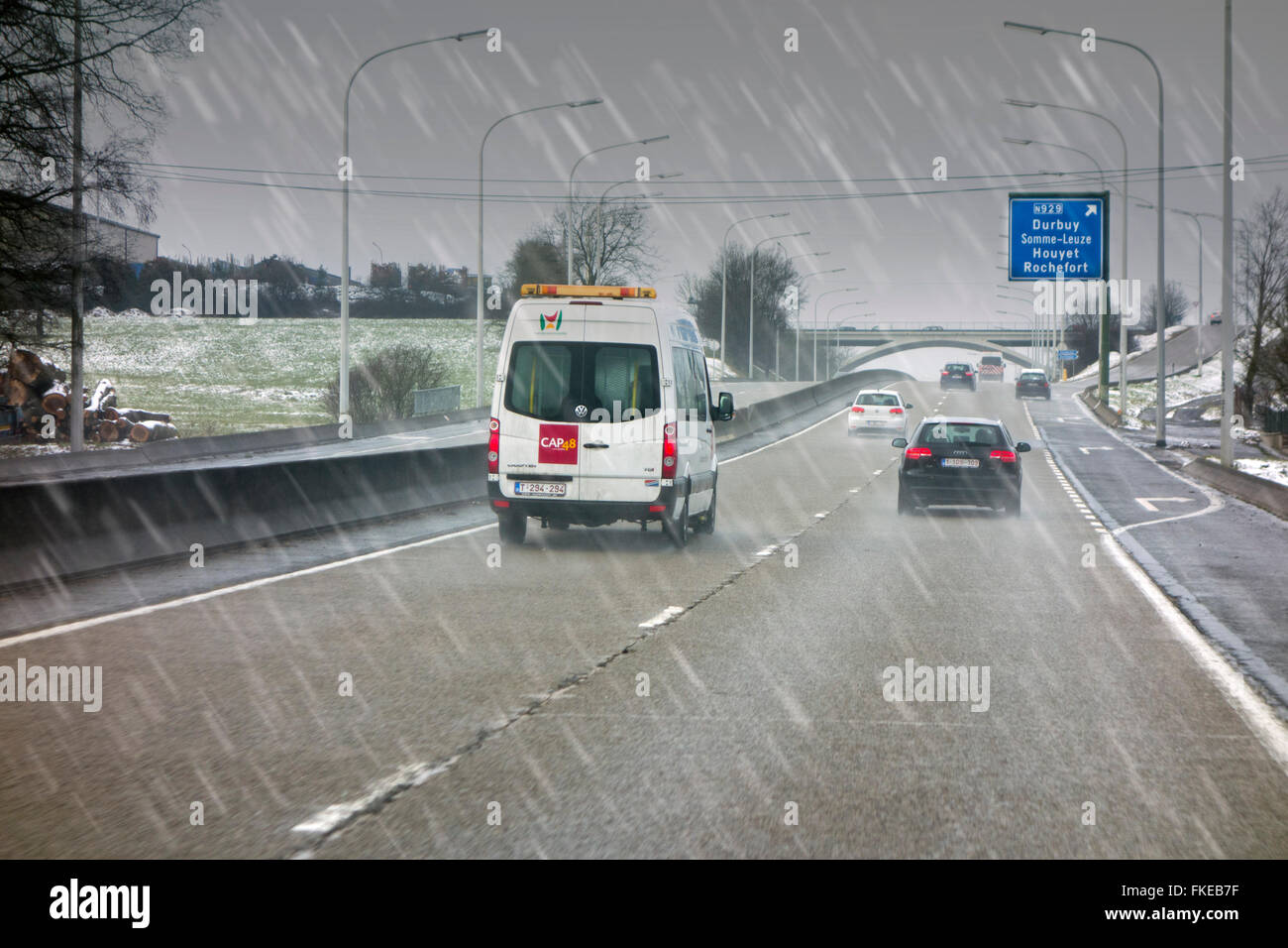 Van il sorpasso di vetture guida su autostrada sdrucciolevoli durante il nevischio causando pericolosi invernale sul bagnato in inverno / molla Foto Stock