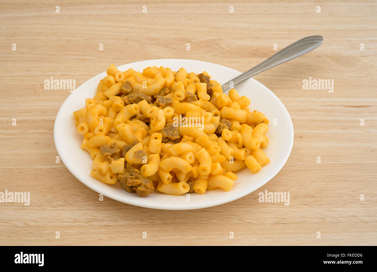 Vista laterale di una forcella inserita nei maccheroni e formaggio con hamburger pezzi su una piastra bianca in cima a una tavola di legno alto. Foto Stock