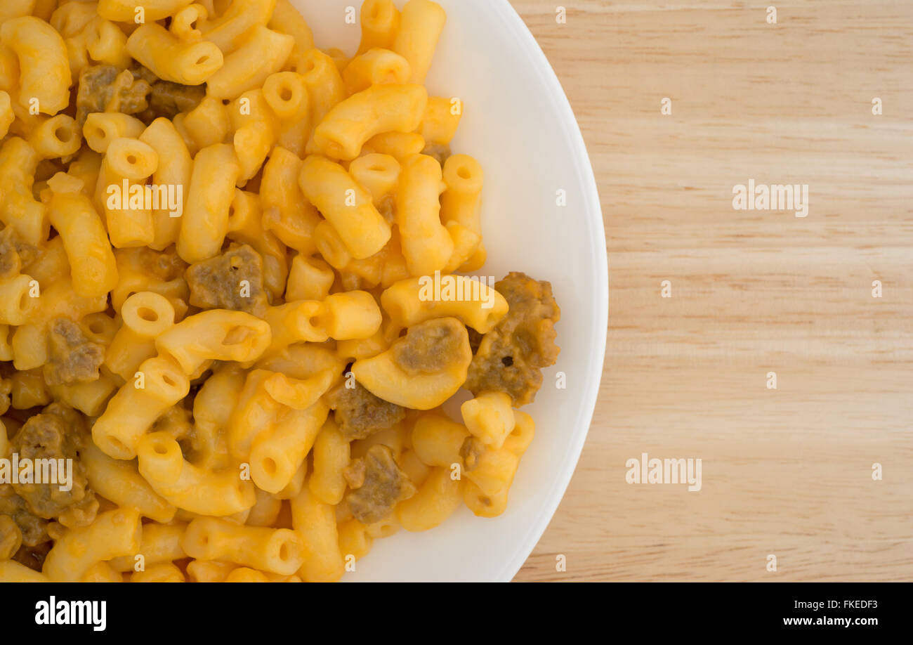 Top vista ravvicinata di maccheroni e formaggio con hamburger pezzi su una piastra bianca in cima a una tavola di legno alto. Foto Stock