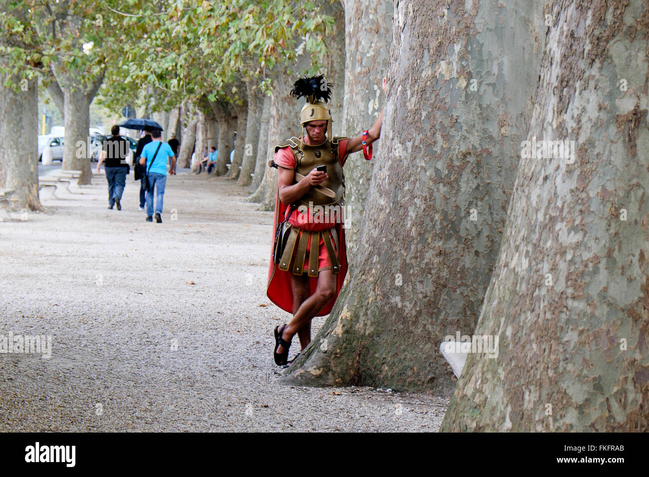 Un attore che ritrae un gladiatore romano si ferma a controllare il suo cellulare nel centro di Roma, in Italia Foto Stock
