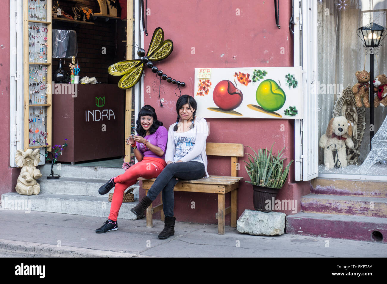 2 impertinente giovane messicano shop famigli ragazze sedersi fuori sul marciapiede bancone di novità boutique dove lavorano Oaxaca Foto Stock