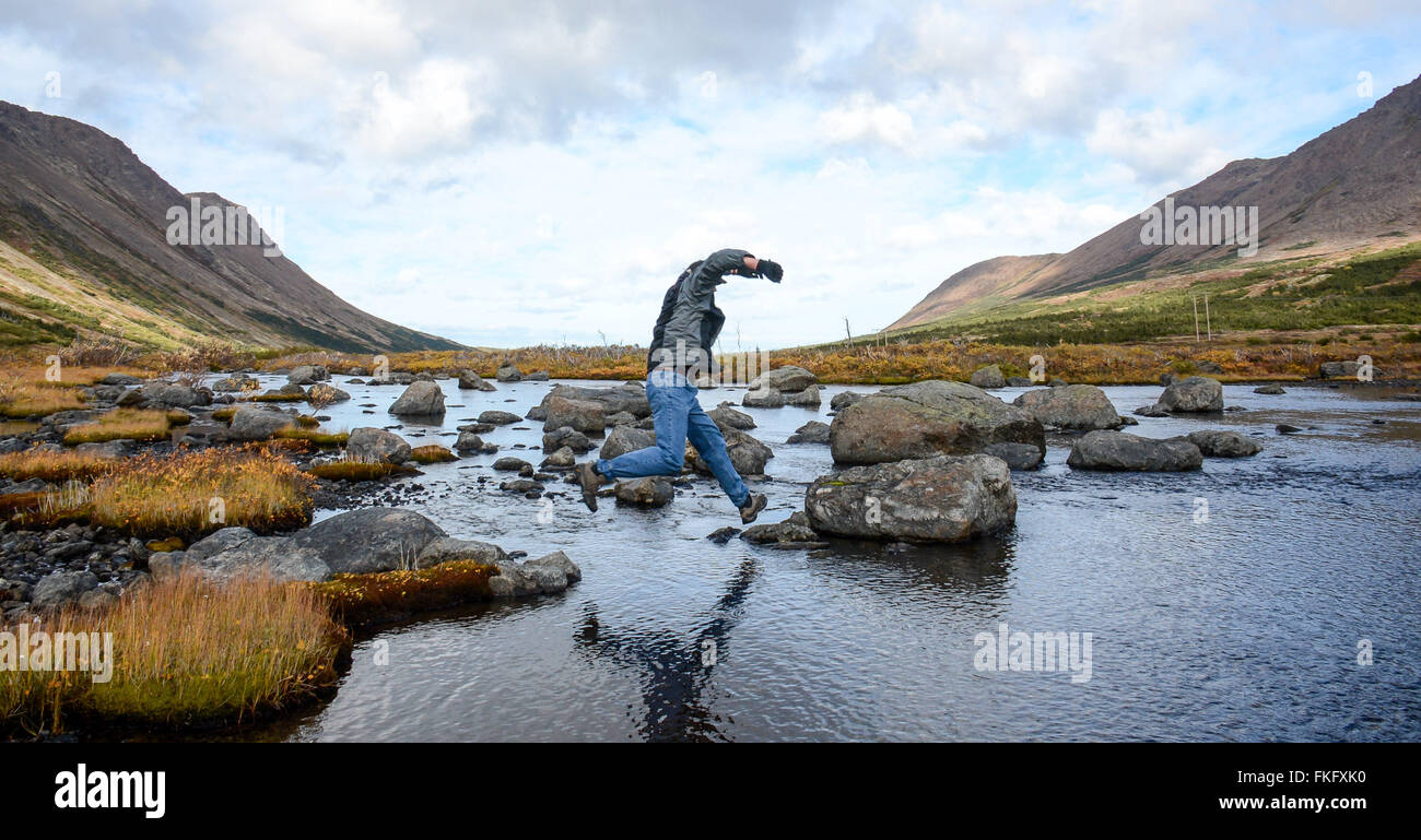 Uomo attraversa creek saltando forma rock rock Foto Stock