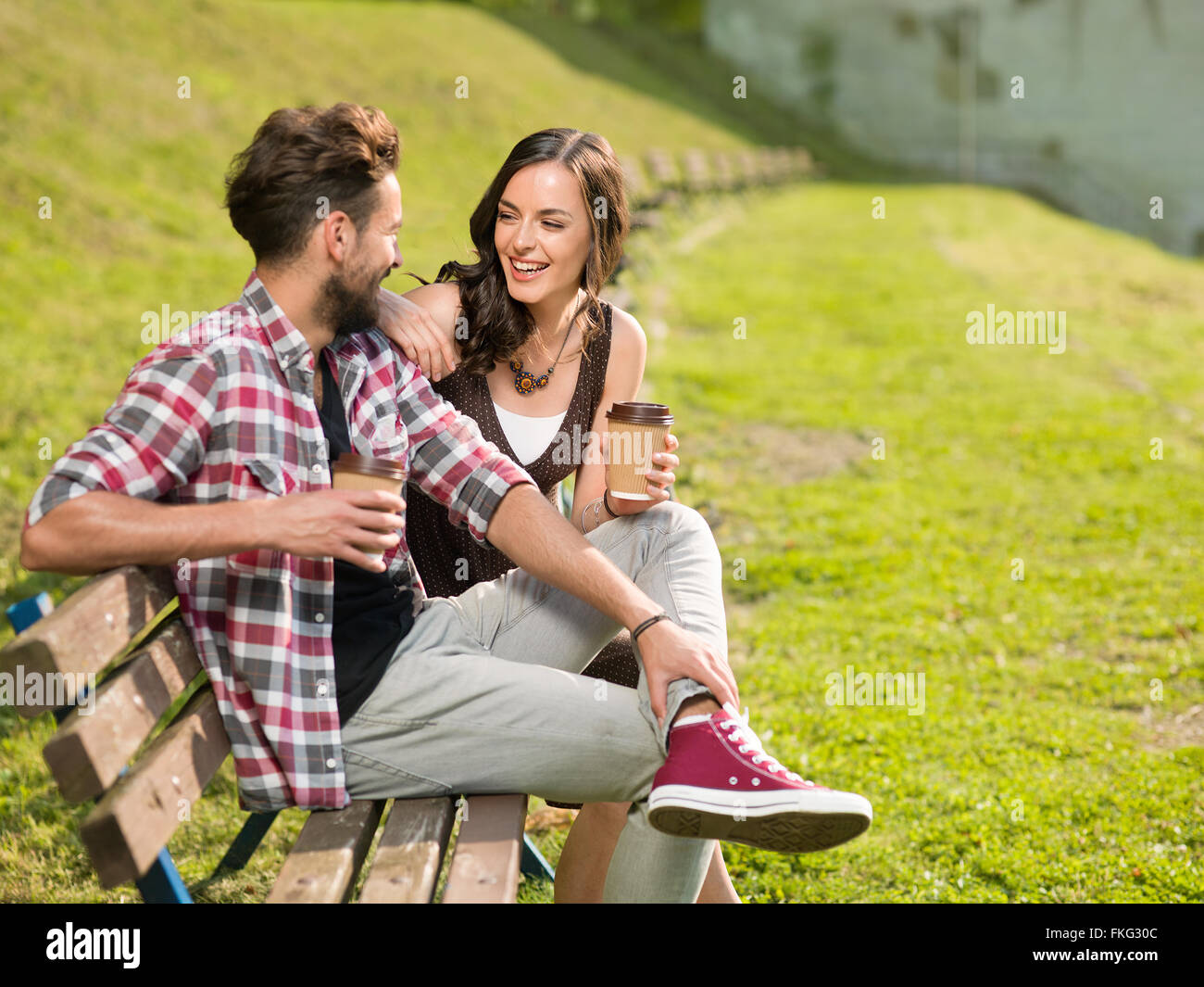 Assapora la sua caffè Bella coppia Giovane su una panchina nel parco di ridere e divertito Foto Stock