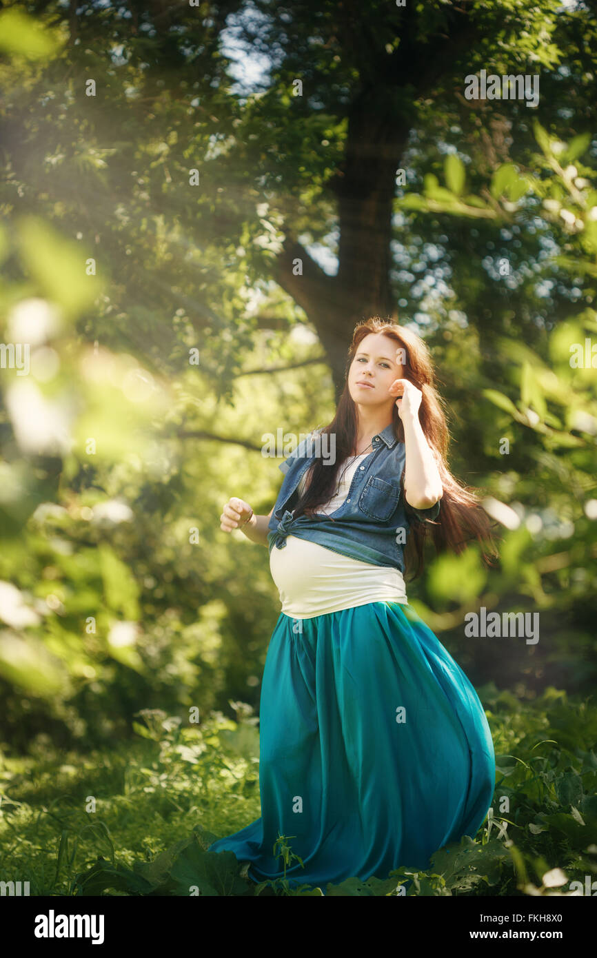 Bella donna incinta in vestito blu per godersi la natura e sole in estate verde parco. A piena altezza verticale, cercando nella fotocamera. Foto Stock