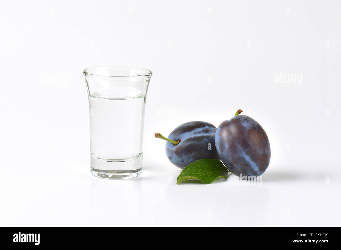 Slivovitz (brandy alla prugna) e prugna fresca su sfondo bianco Foto Stock