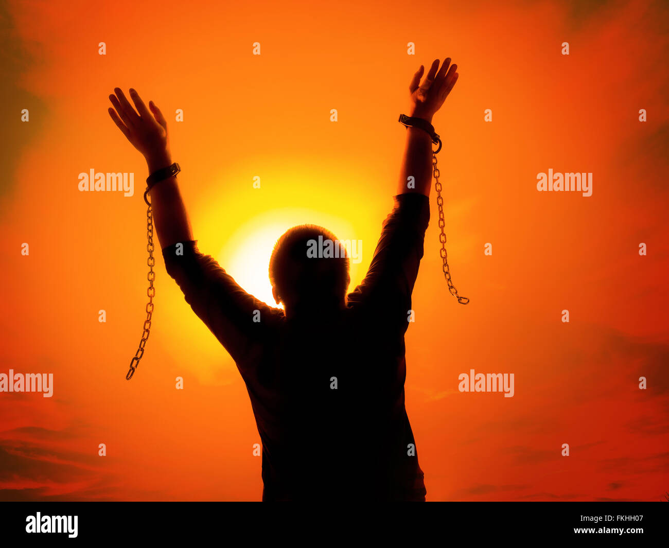 Silhouette di uomo contro il Cielo di tramonto alzando le mani come egli diventa libero dalle catene e anelli portagancio Foto Stock