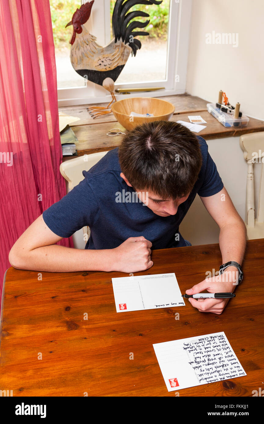 Un ragazzo di 15 anni scrive una cartolina dalla sua famiglia in vacanza nel Regno Unito Foto Stock