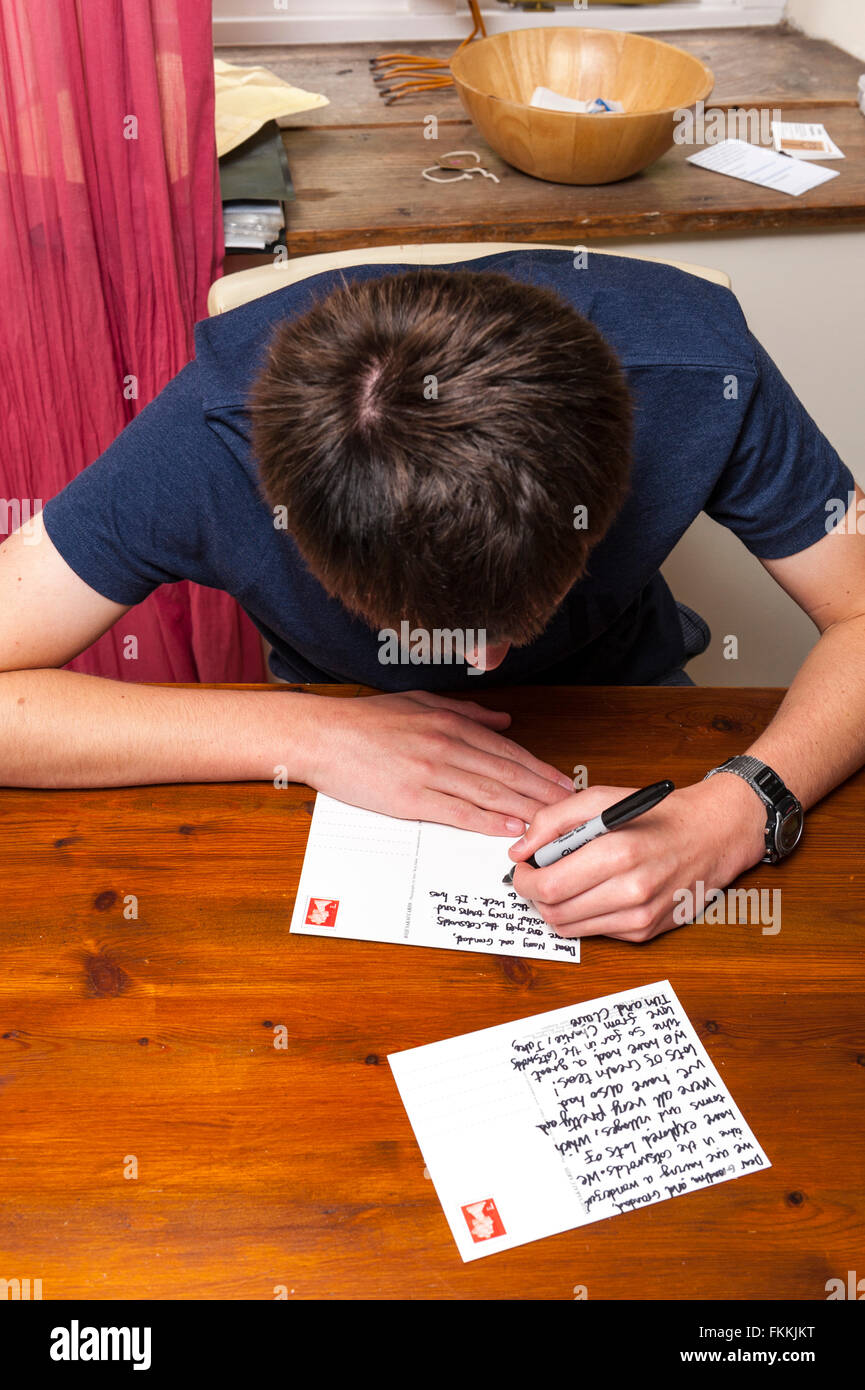 Un ragazzo di 15 anni scrive una cartolina dalla sua famiglia in vacanza nel Regno Unito Foto Stock