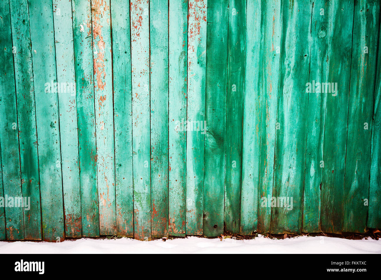 Peeling vernice verde sulla weathered asse di legno recinzione e un suolo coperto di neve Foto Stock