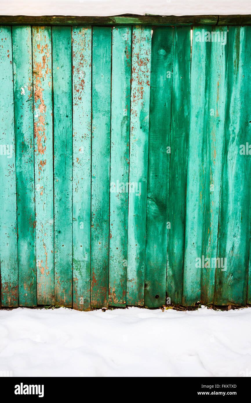 Peeling vernice verde sulla weathered asse di legno recinzione e un suolo coperto di neve Foto Stock