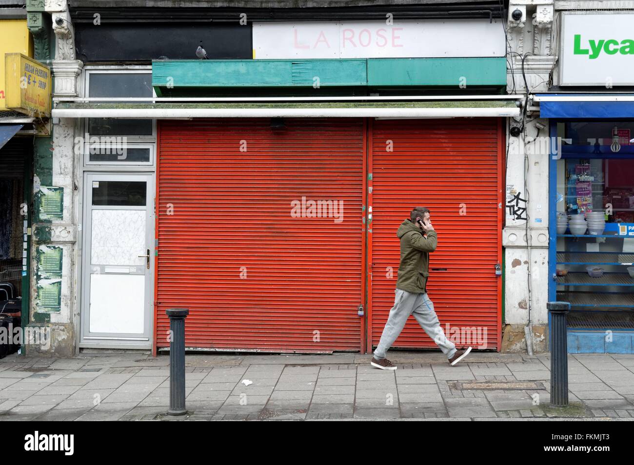 Uomo al telefono a piedi da un negozio chiuso in Harlesden London REGNO UNITO Foto Stock