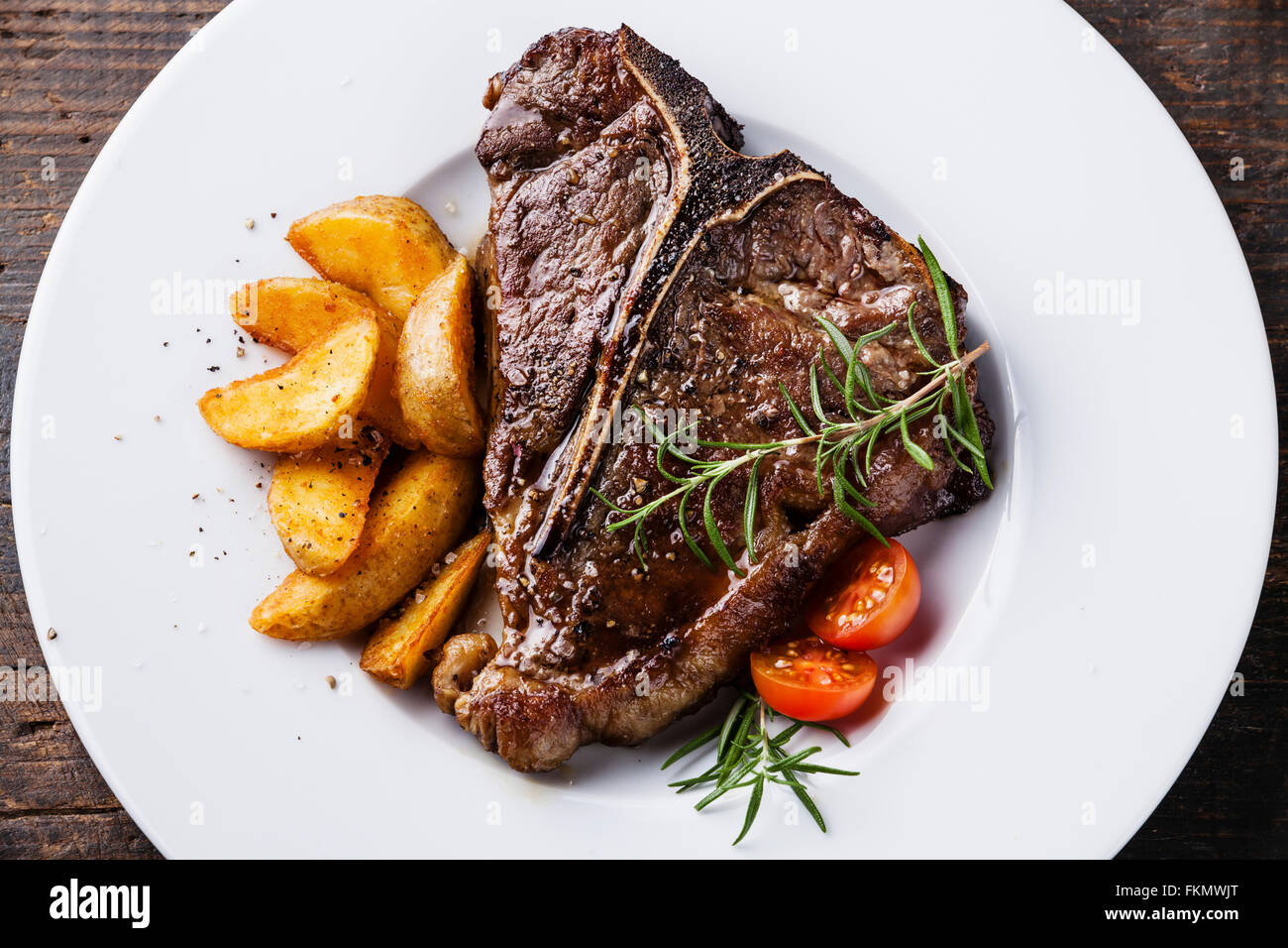 Grigliata di T-Bone Steak con patate arrosto cunei su piastra bianca su sfondo di legno vicino fino Foto Stock