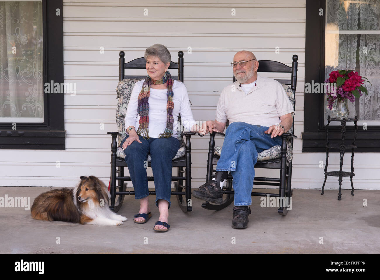 Un anziana coppia di sposi nel loro ottanta guardate il mondo passare da loro portico con il loro cane sheltie al loro fianco. Foto Stock