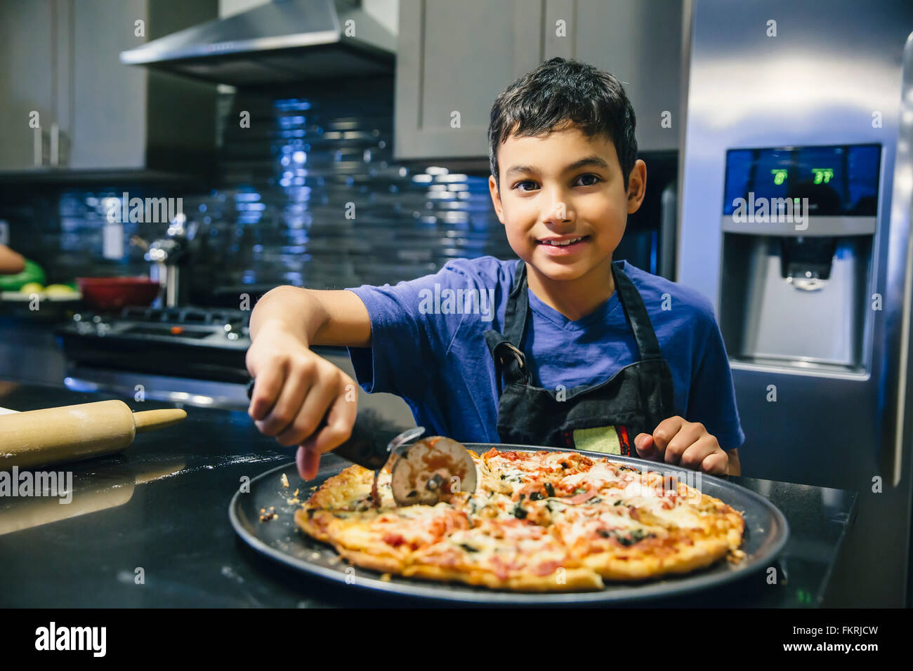 Razza mista ragazzo per affettare la pizza in cucina Foto Stock