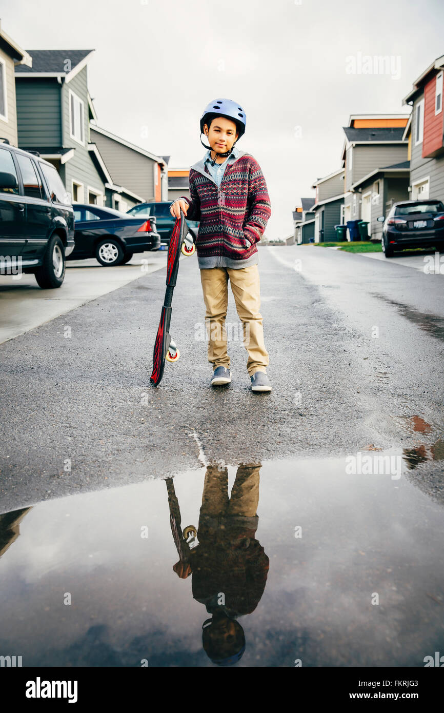 Razza mista ragazzo con lo skateboard riflessa nella pozzanghera Foto Stock