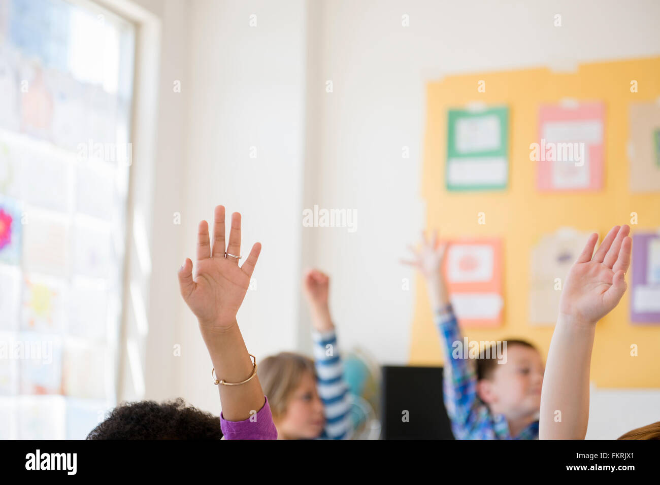 Gli studenti alzando le mani in aula Foto Stock