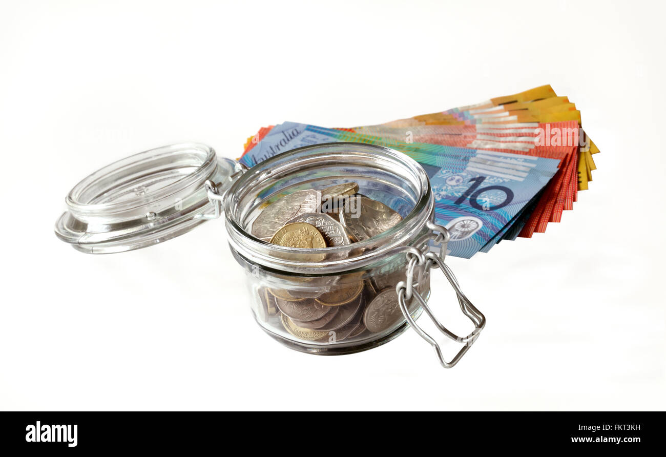 Australian banconote posa dietro un piccolo vasetto di vetro che contiene monete australiana, tutti mostrato su uno sfondo bianco Foto Stock