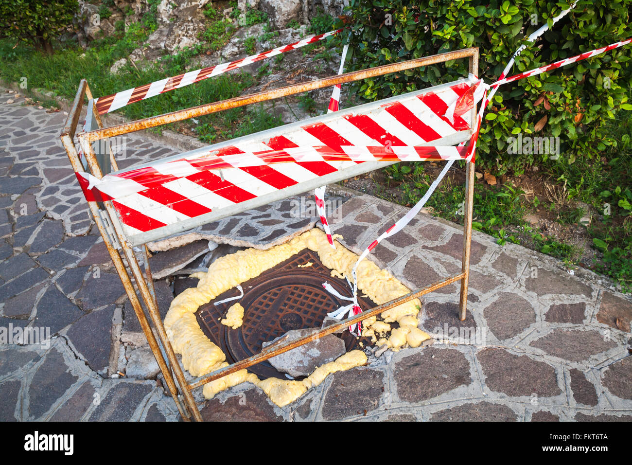 Strada urbana in costruzione, a strisce rosse e bianche vicino alla barriera rotto tombino fognario il portello è fissato con schiuma Foto Stock